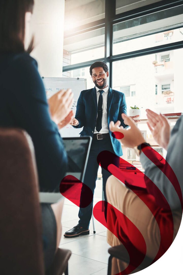 A man in a suit applauding in a bright office meeting.