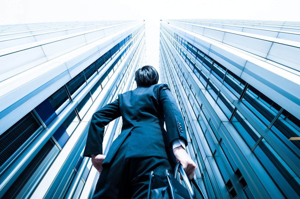 Businessman looking up at tall glass skyscrapers on a bright day.