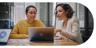Two women collaborating on a laptop in a modern workspace.