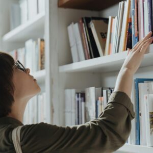 A woman reaching for a book on a white bookshelf.