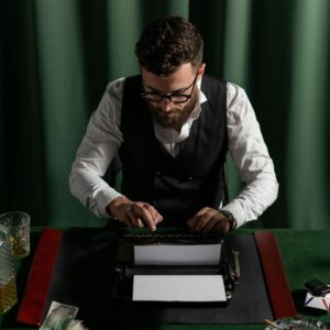 Man intensely using a typewriter in a dimly lit room with green curtains.