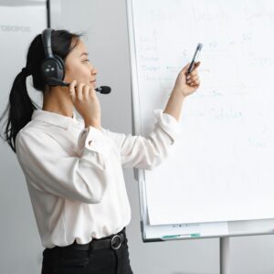 A businesswoman wearing a headset presenting with a whiteboard.