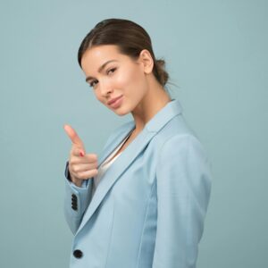 A confident woman in a light blue blazer points forward with a playful expression.