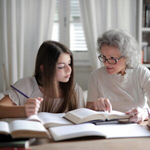 An elderly woman and a young girl studying together with books.