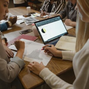 People collaborating with documents and laptop at a wooden table.