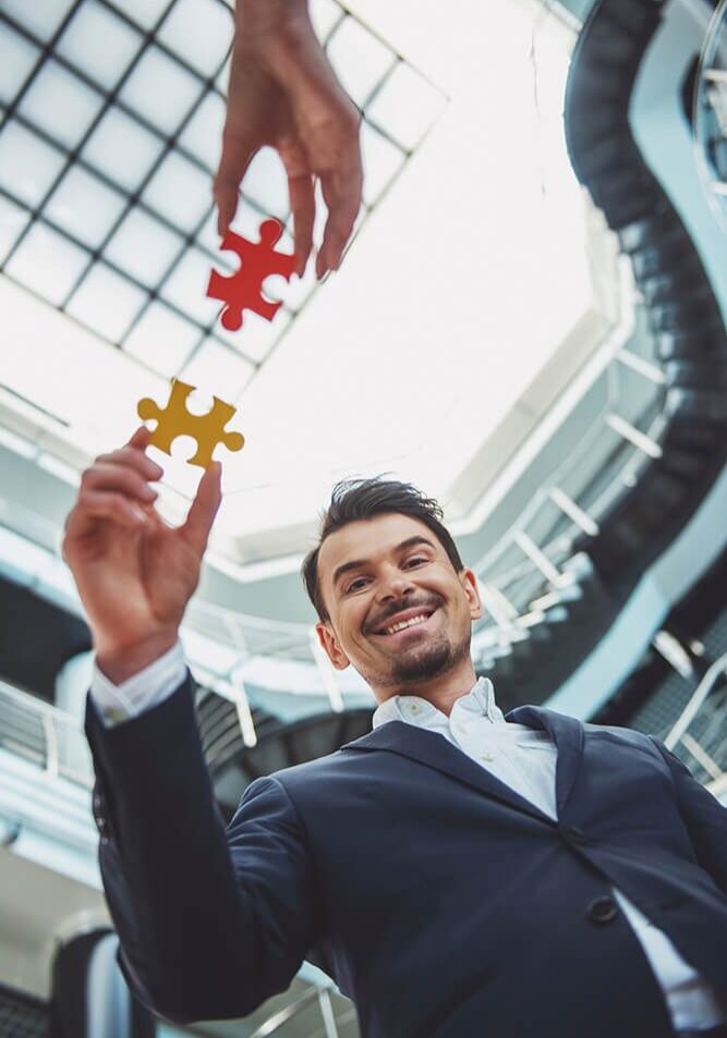 A businessman holding two puzzle pieces about to connect them.