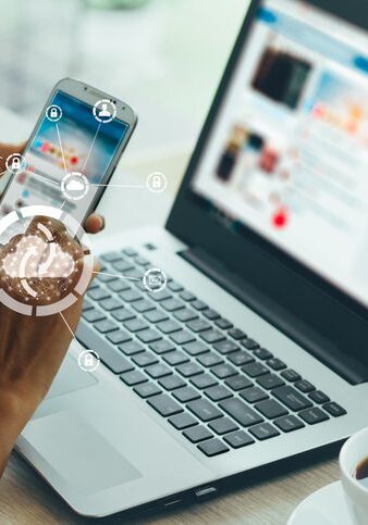 Person holding a smartphone showing a smartwatch app near an open laptop.