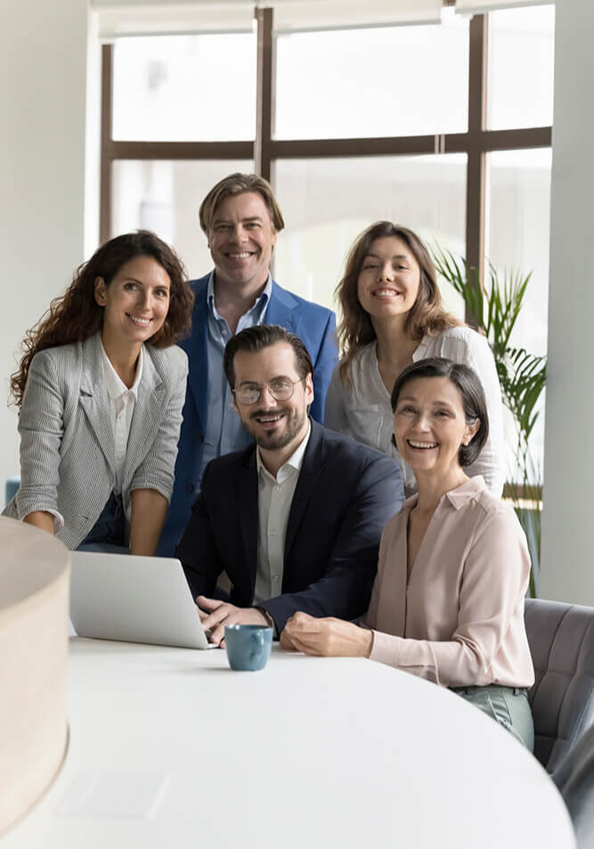 Five professionals smiling together in an office setting.