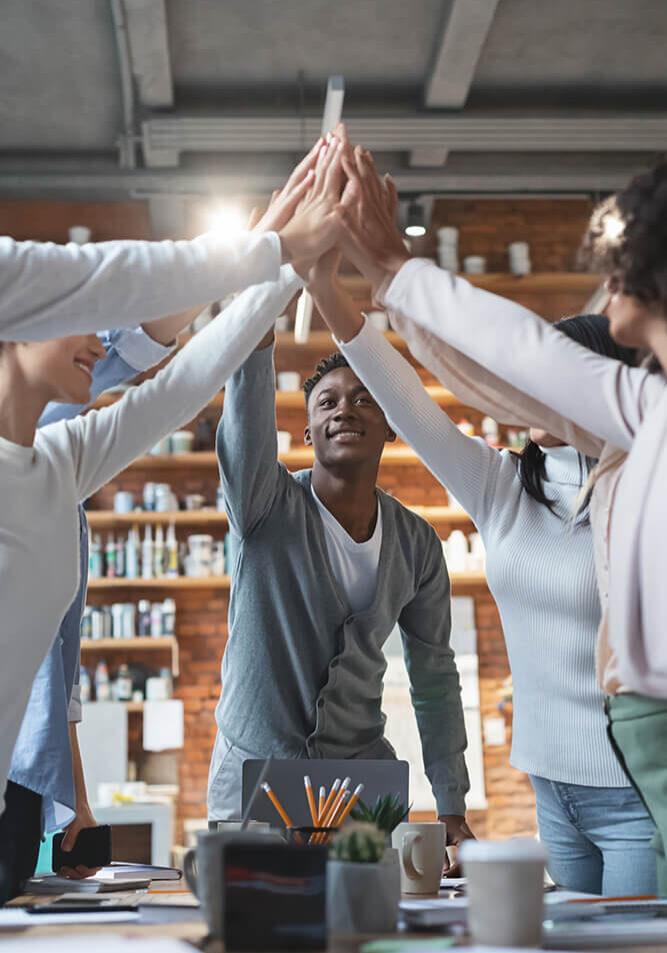 A diverse group celebrates with a group high-five in a cozy workspace.