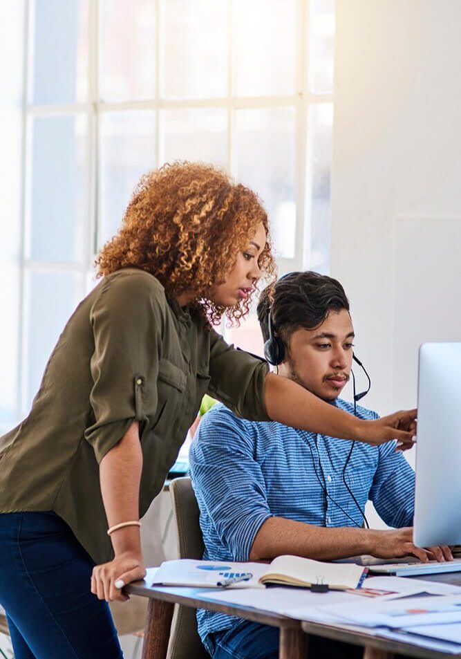 Two colleagues collaborating on a project at a computer in a bright office.