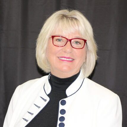 Portrait of a woman with blonde hair and red glasses smiling.