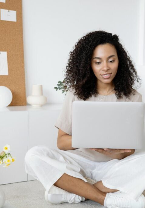 Young woman sitting on floor working on laptop, smiling.
