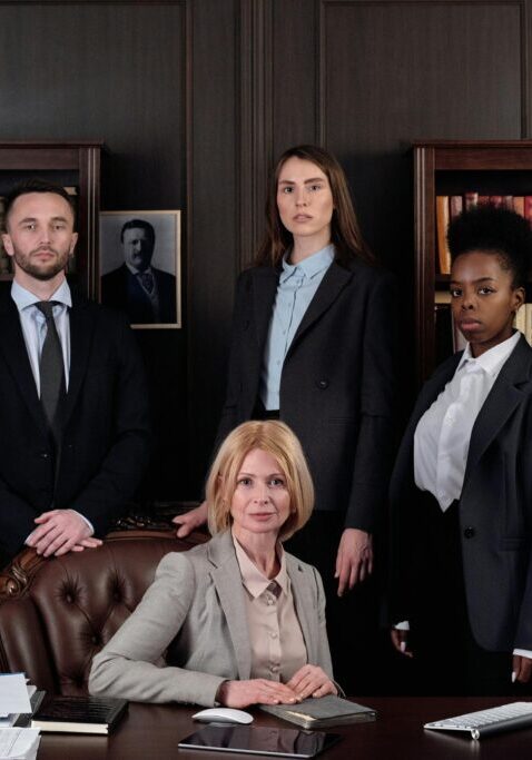 A professional business team posing in an office with a seated leader.