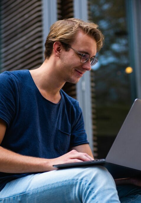 Young man working on a laptop outdoors, smiling.