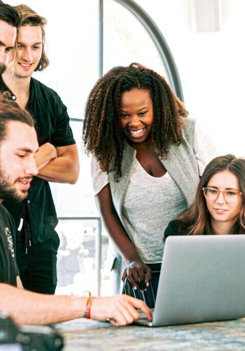 A diverse group collaborating enthusiastically around a laptop in a modern workspace.