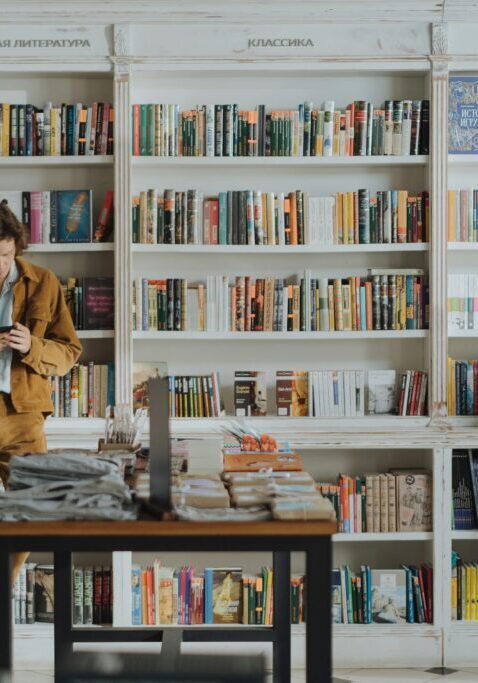 Two people browsing books in a cozy bookstore with white shelves.