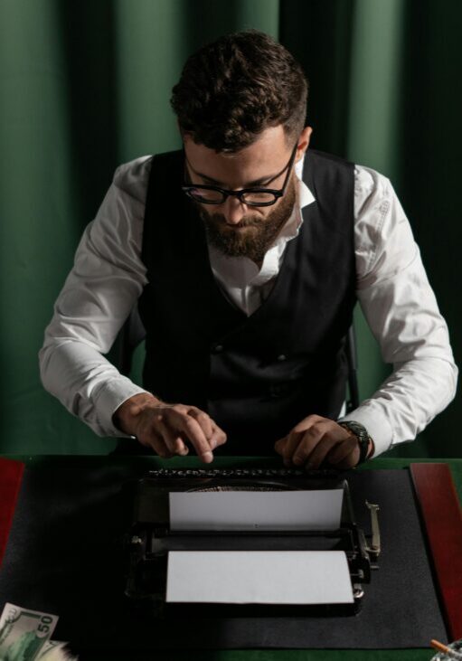 Man intensely using a typewriter in a dimly lit room with green curtains.