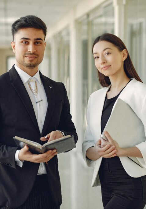 Two professionals standing in a modern office hallway with tablets.