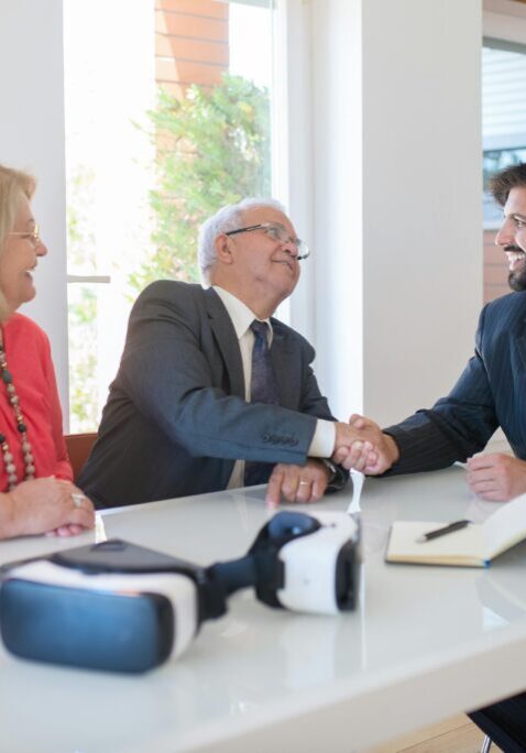 Two men shaking hands in a business meeting with a woman observing.