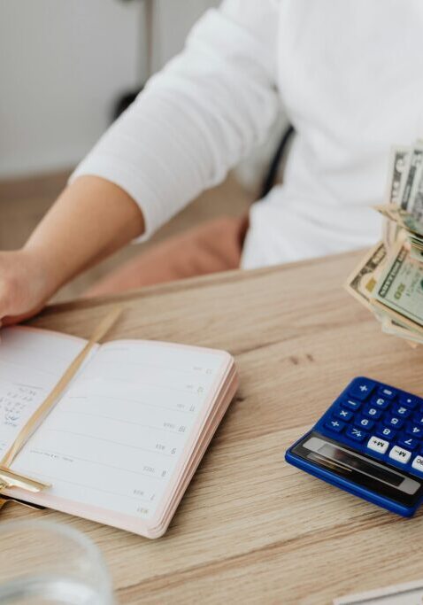 Person budgeting with cash, calculator, and notebook.