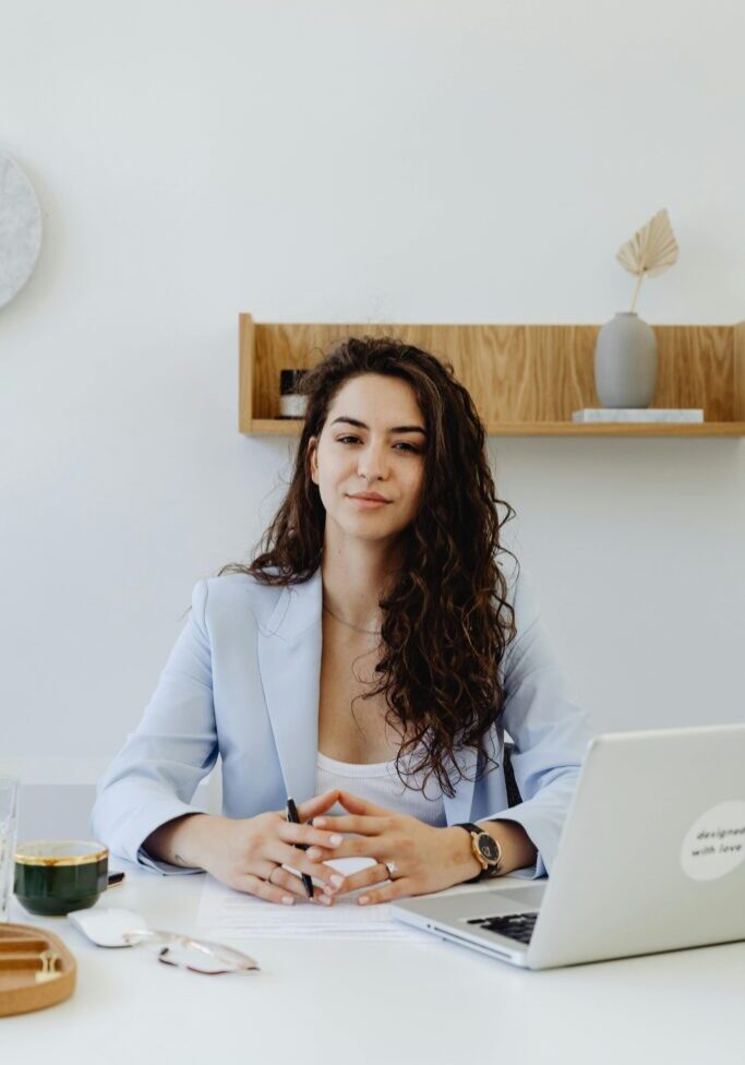 Confident woman with curly hair in a light blazer at her workspace.