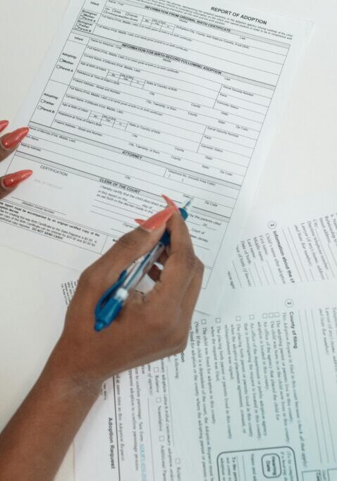 Person filling out forms with a pen on a white table.
