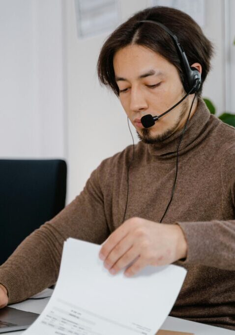 Woman working in a call center, reviewing documents with headset on.