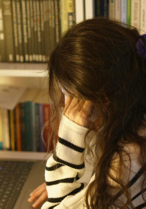 A person focused on a laptop with bookshelves in the background.