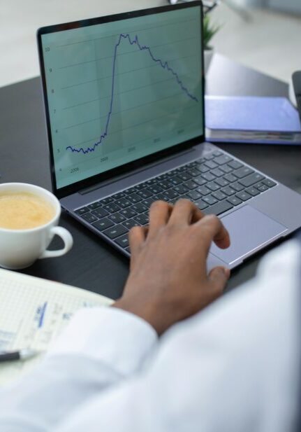 Person analyzing financial data on laptop and tablet with coffee nearby.
