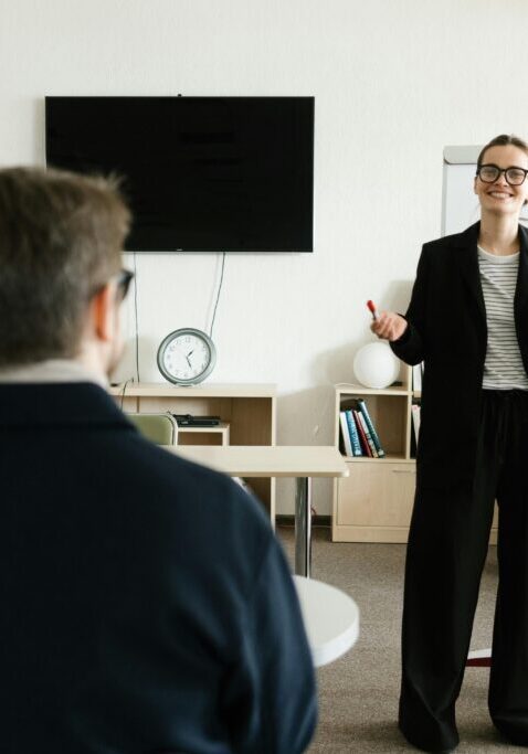 A woman giving a presentation to a seated man in a modern office.