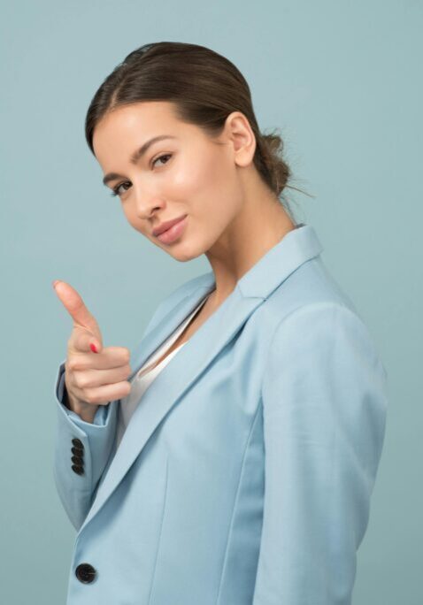 A confident woman in a light blue blazer points forward with a playful expression.