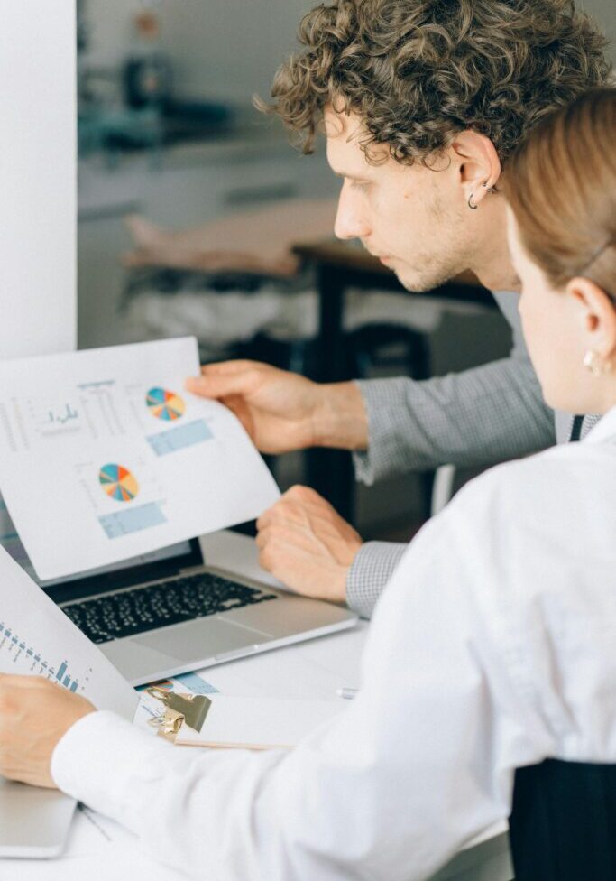 Two professionals reviewing charts on a laptop during a meeting.