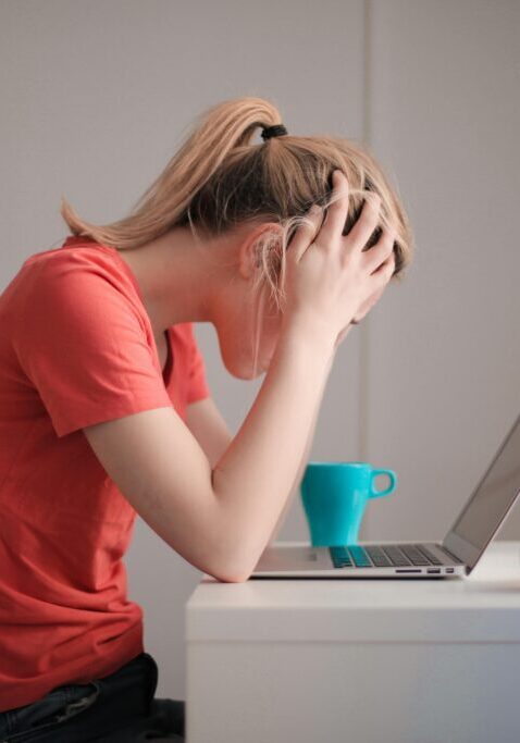 Stressed woman holding her head in front of a laptop.