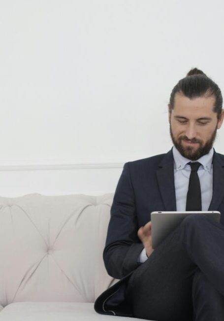 Man in a suit reading a document on a couch.