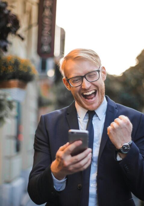 Excited businessman celebrating success with a fist pump and phone.