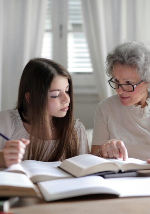 An elderly woman and a young girl studying together with books.