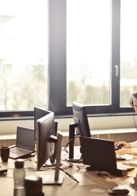 Two men working at computers in a bright office with large windows.