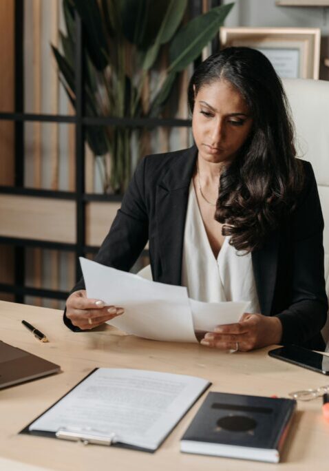 Professional woman reviewing documents at her desk in a modern office.