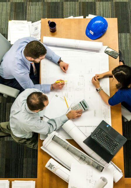 Three professionals collaborating over blueprints and documents in a workspace.