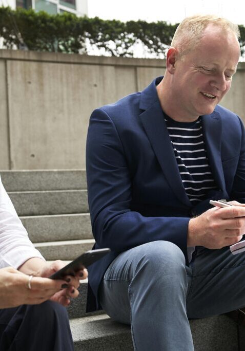 Two men sitting outdoors, one writing on a notebook.