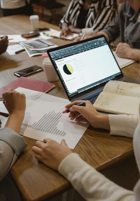 People collaborating with documents and laptop at a wooden table.